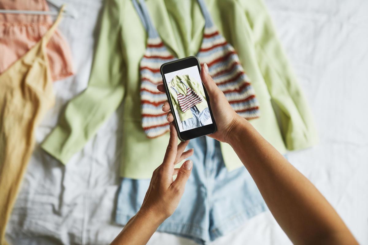 Persona fotografiando con su celular prendas de ropa extendidas sobre una cama